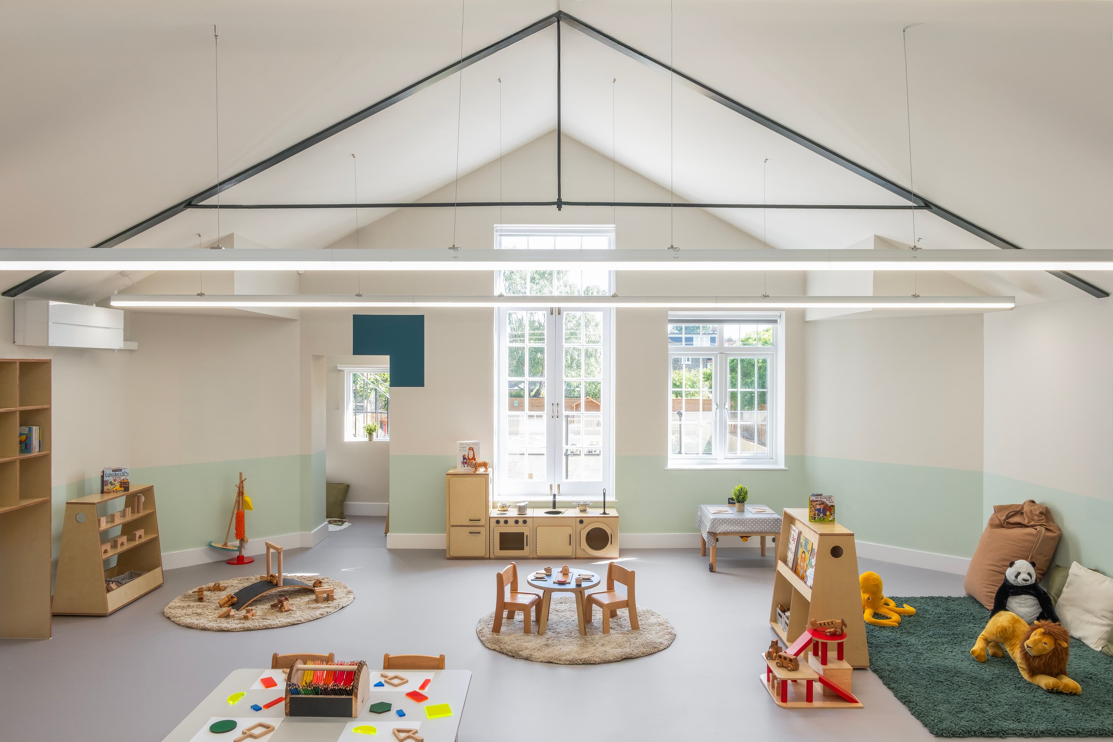A bright, modern children's playroom with a vaulted ceiling, light walls, and diverse activity zones featuring toys and small furniture.
