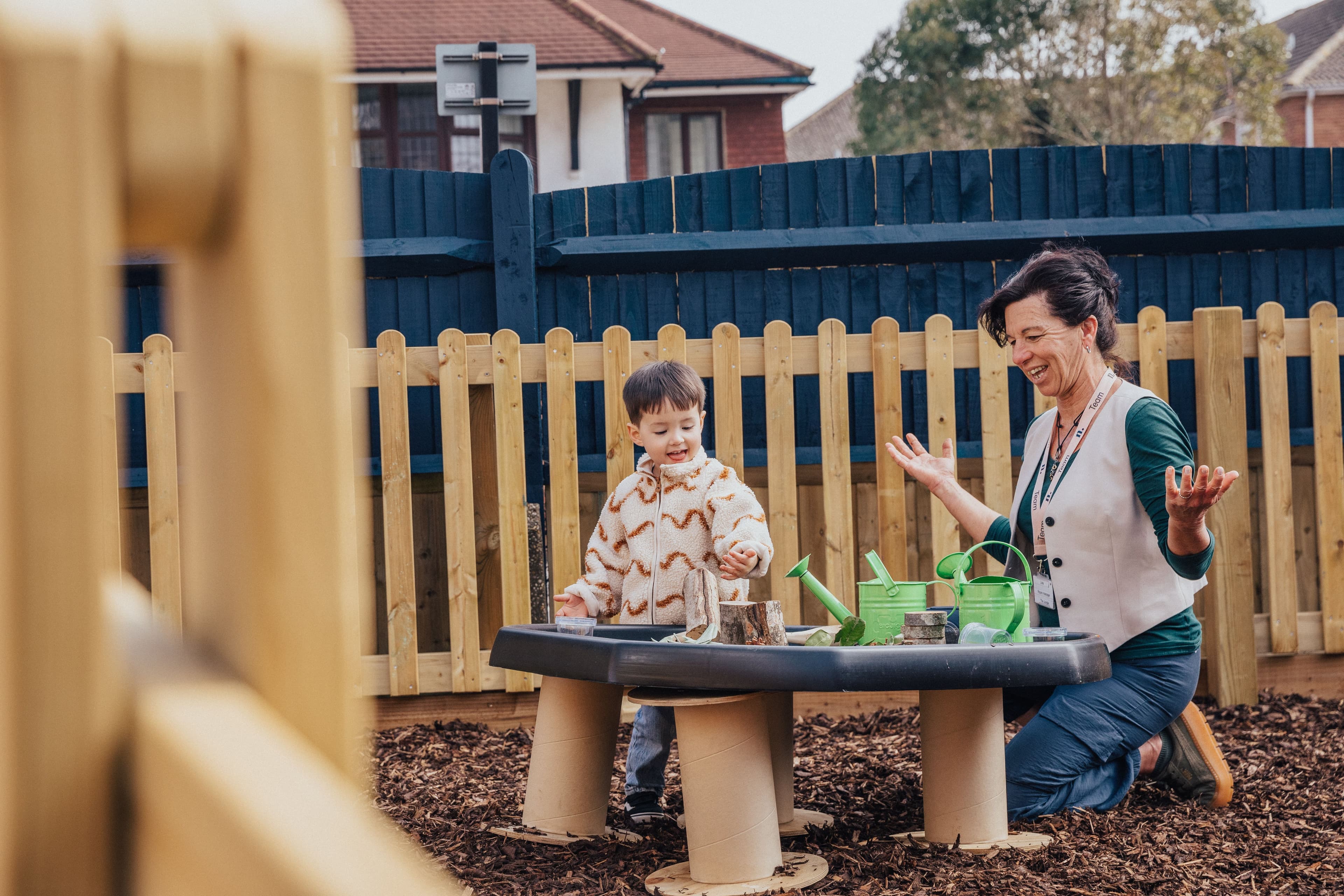 A child and an adult play outdoors at a sensory table with watering cans.